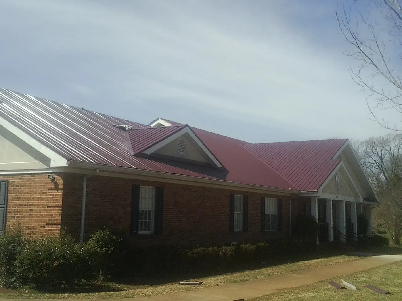 Red metal roof with gabled entries on a long brick building, from a Hail Damage Roof Repair job in Republic
